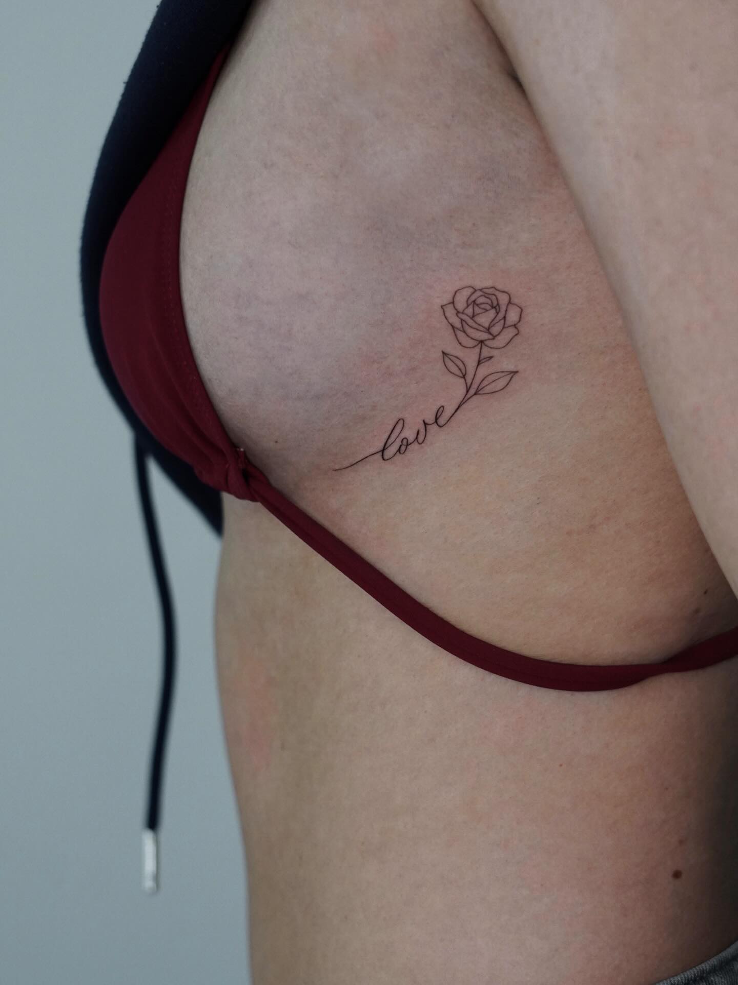Fineline-Rose mit Schriftzug „love“ an der Rippe, gestochen von Max